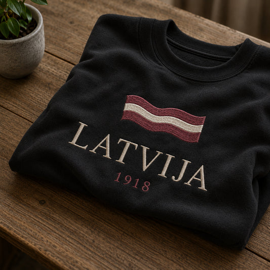 Melns salocīts džemperis ar “Latvija 1918” izšuvumu plašākā plakanā izkārtojuma kopskatā