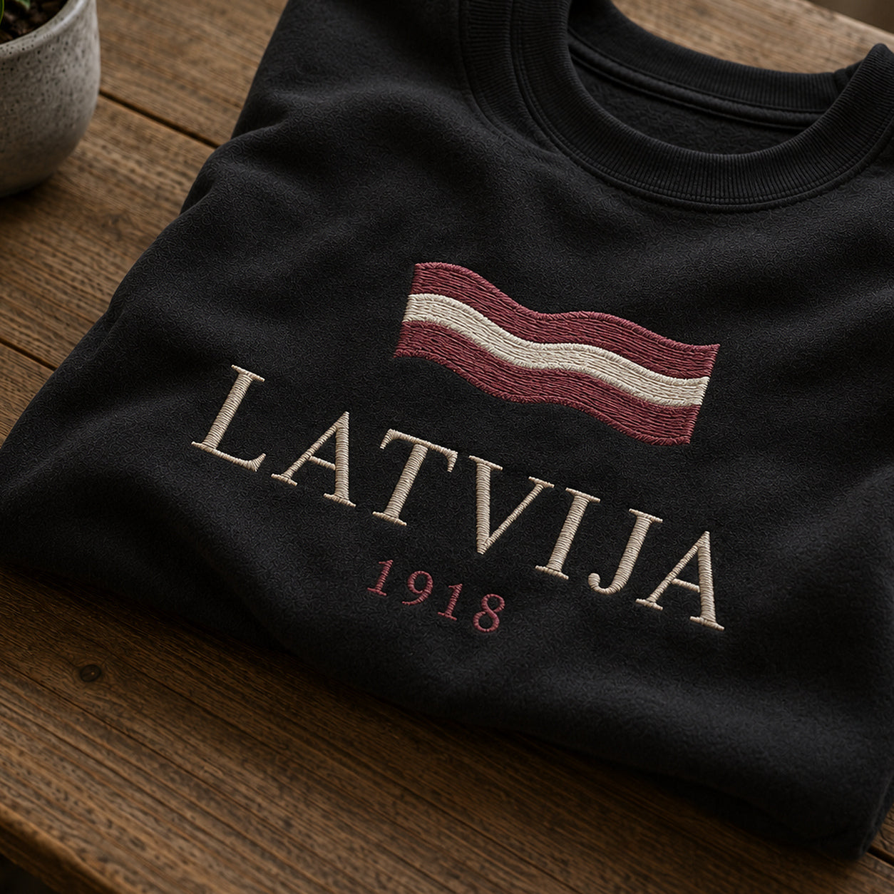 Tuvāks “Latvija 1918” kompozīcijas skats uz melnu salocītu džemperi ar tekstu “Latvija” un apakštekstu “1918”