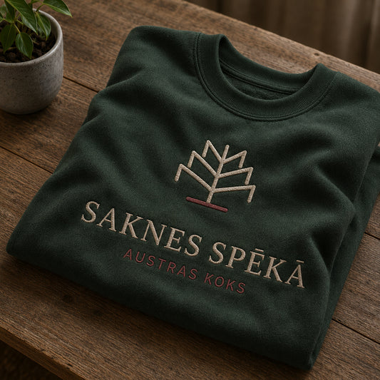 Meža zaļš salocīts džemperis ar “Saknes spēkā” izšuvumu plašākā plakanā izkārtojuma kopskatā