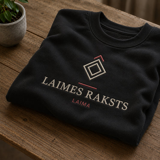 Melns salocīts džemperis ar “Laimes raksts” izšuvumu plašākā plakanā izkārtojuma kopskatā