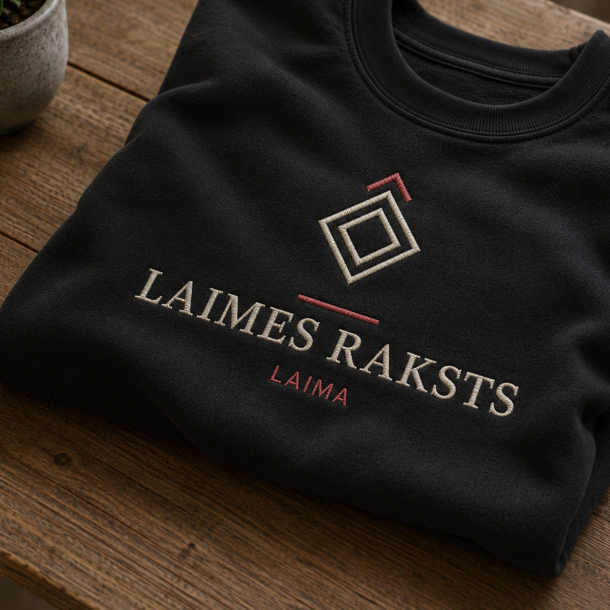 Tuvāks “Laimes raksts” kompozīcijas skats uz melnu salocītu džemperi ar tekstu “Laimes raksts” un apakštekstu “Laima”