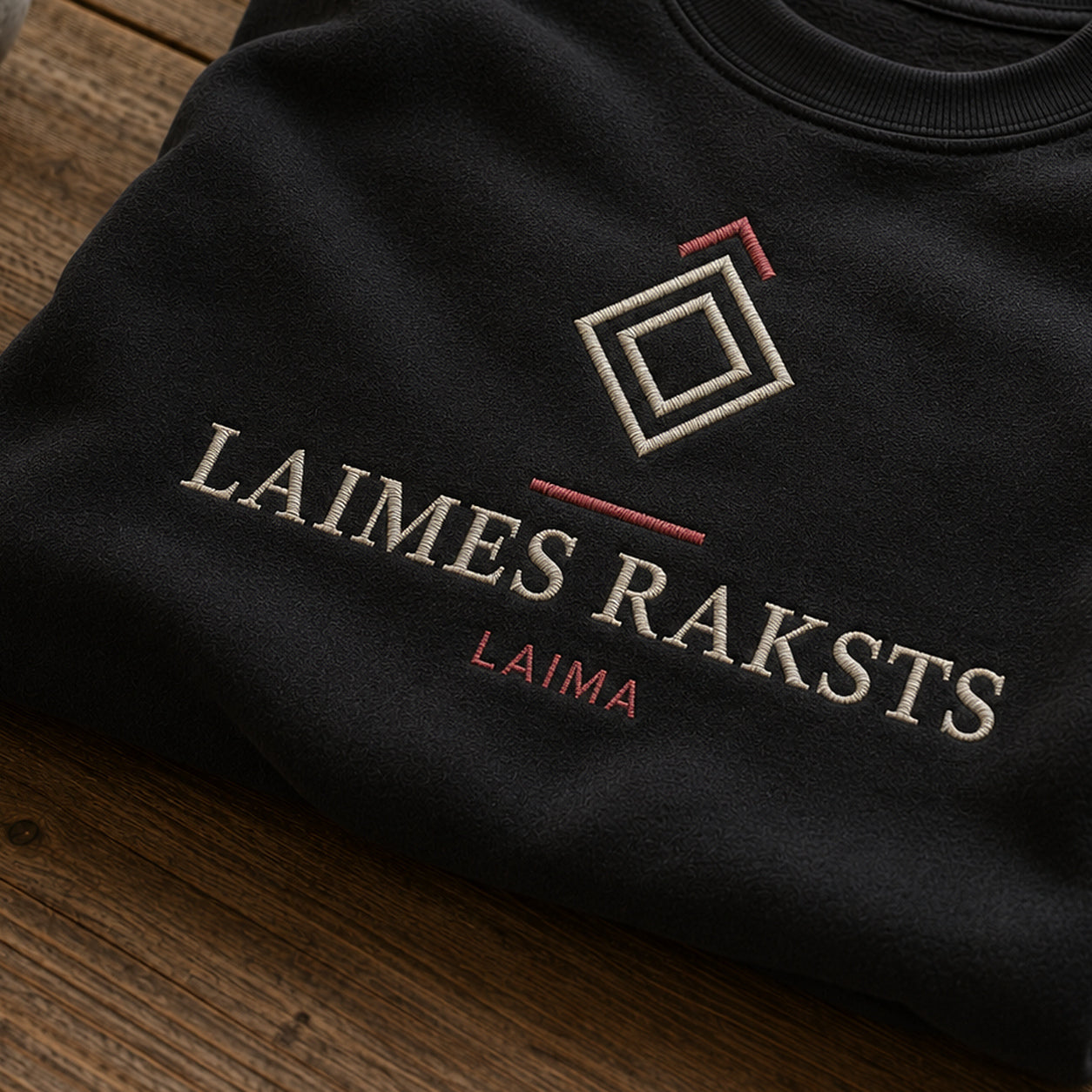 “Laimes raksts” izšuvuma detaļu tuvplāns uz melna džempera auduma, redzams motīvs: Laimas zīmes raksts un vēlējums Laimes raksts