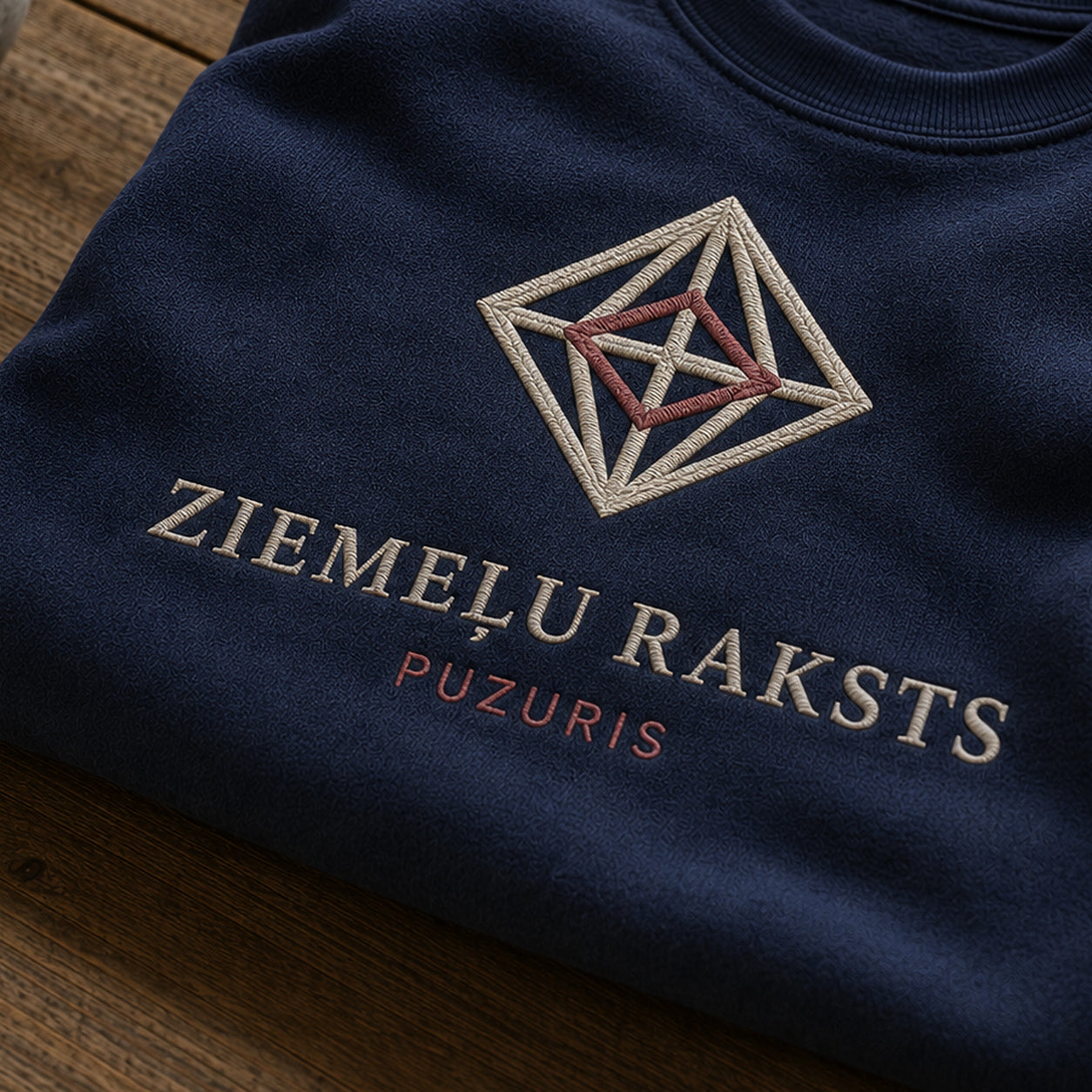 “Ziemeļu raksts” izšuvuma detaļu tuvplāns uz tumši zila džempera auduma, redzams motīvs: puzura precīzā telpiskuma iespaids un vārdi Ziemeļu raksts