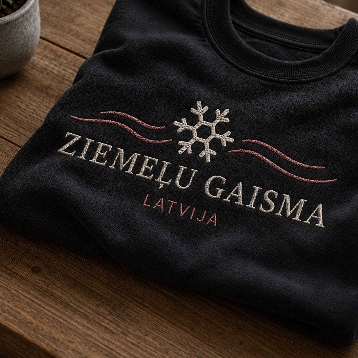 Tuvāks “Ziemeļu gaisma” kompozīcijas skats uz melnu salocītu džemperi ar tekstu “Ziemeļu gaisma” un apakštekstu “Latvija”