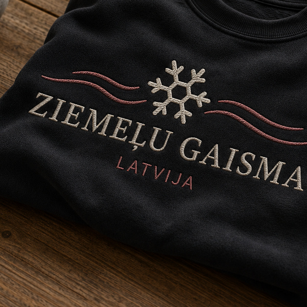 “Ziemeļu gaisma” izšuvuma detaļu tuvplāns uz melna džempera auduma, redzams motīvs: noskaņu pilns uzraksts Ziemeļu gaisma ar Latvijas akcentu
