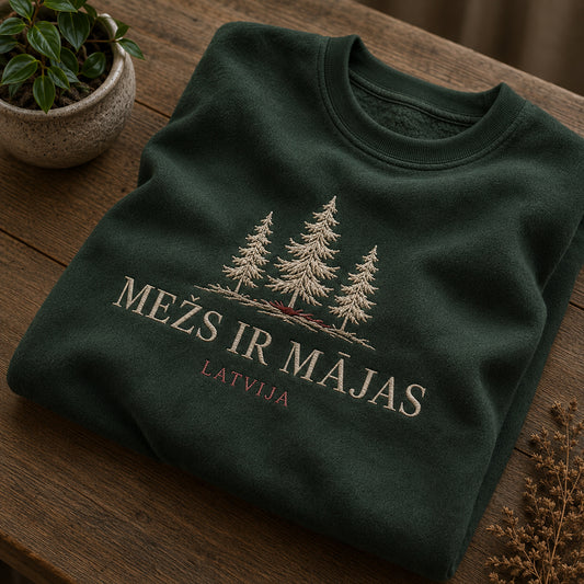 Meža zaļš salocīts džemperis ar “Mežs ir mājas” izšuvumu plašākā plakanā izkārtojuma kopskatā