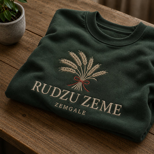 Meža zaļš salocīts džemperis ar “Rudzu zeme” izšuvumu plašākā plakanā izkārtojuma kopskatā