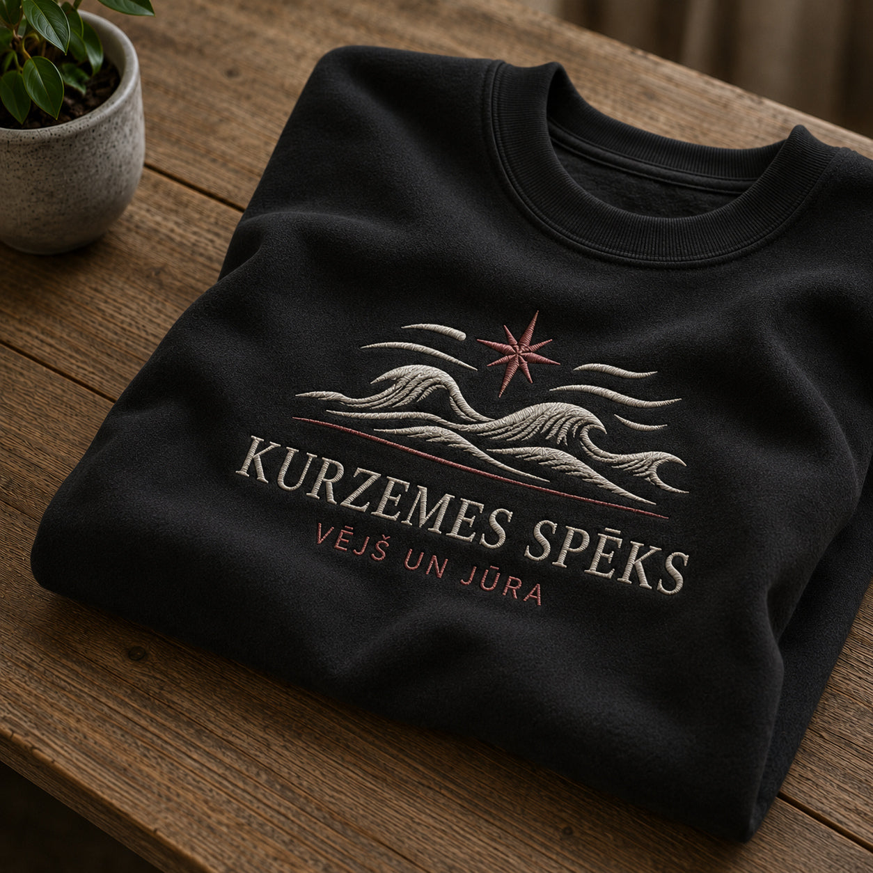 Melns salocīts džemperis ar “Kurzemes spēks” izšuvumu plašākā plakanā izkārtojuma kopskatā