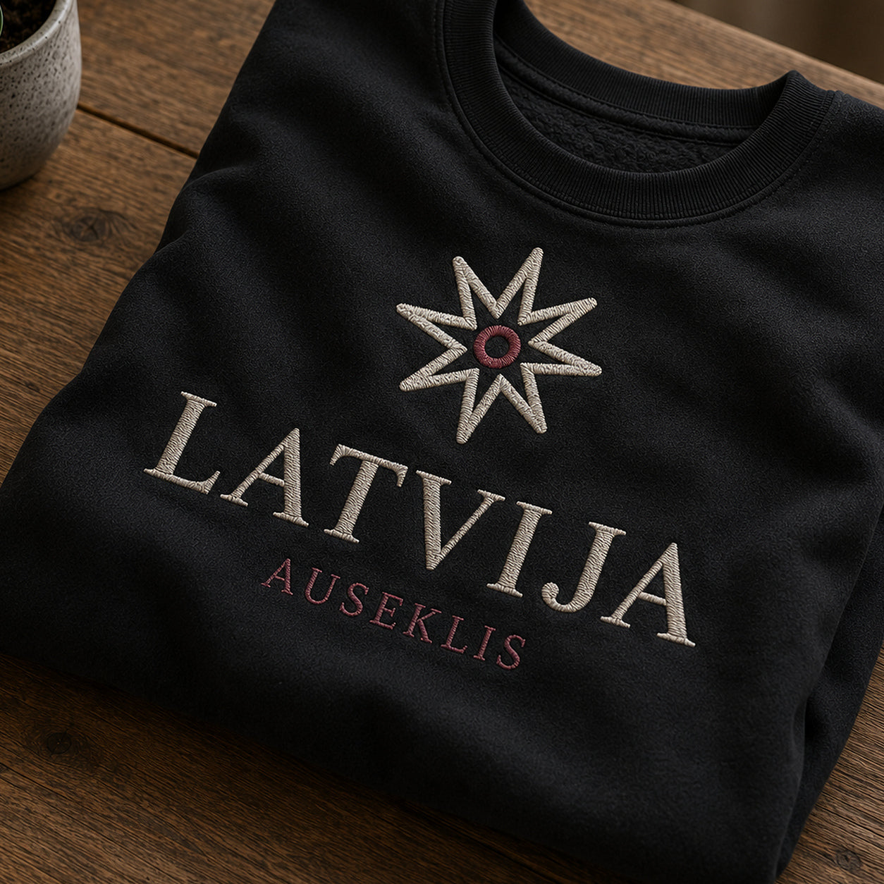 Tuvāks “Auseklis Latvija” kompozīcijas skats uz melnu salocītu džemperi ar tekstu “Latvija” un apakštekstu “Auseklis”